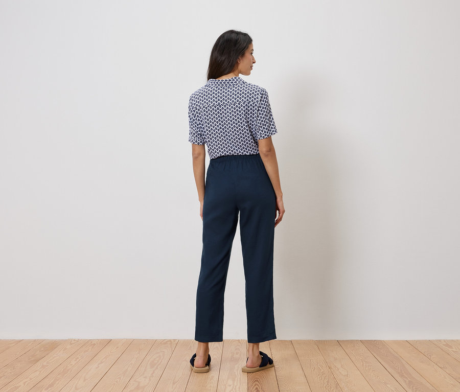 Egy nő áll háttal a kamerának, kék-fehér felsőt és sötétkék nadrágot visel.