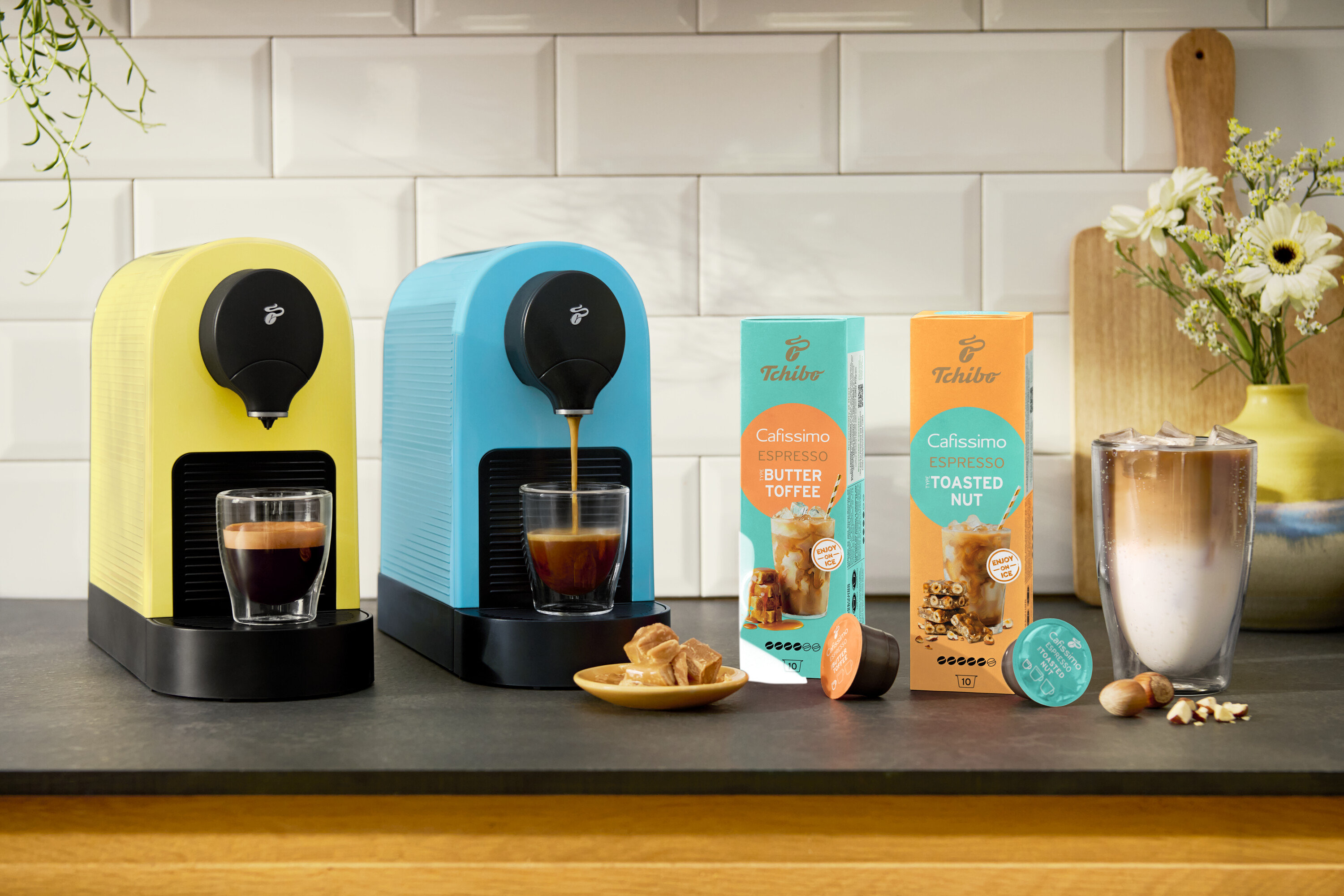 Két Cafissimo pure+ kávéfőző sárga és kék színben eszpresszót készít. Látható még Cafissimo Flavoured Espresso – Toasted Nut kapszula.