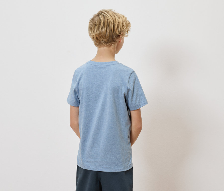 Hátulnézet egy szőke, göndör hajú gyermekről, aki világoskék pólót és sötétkék rövidnadrágot visel fehér háttér előtt.