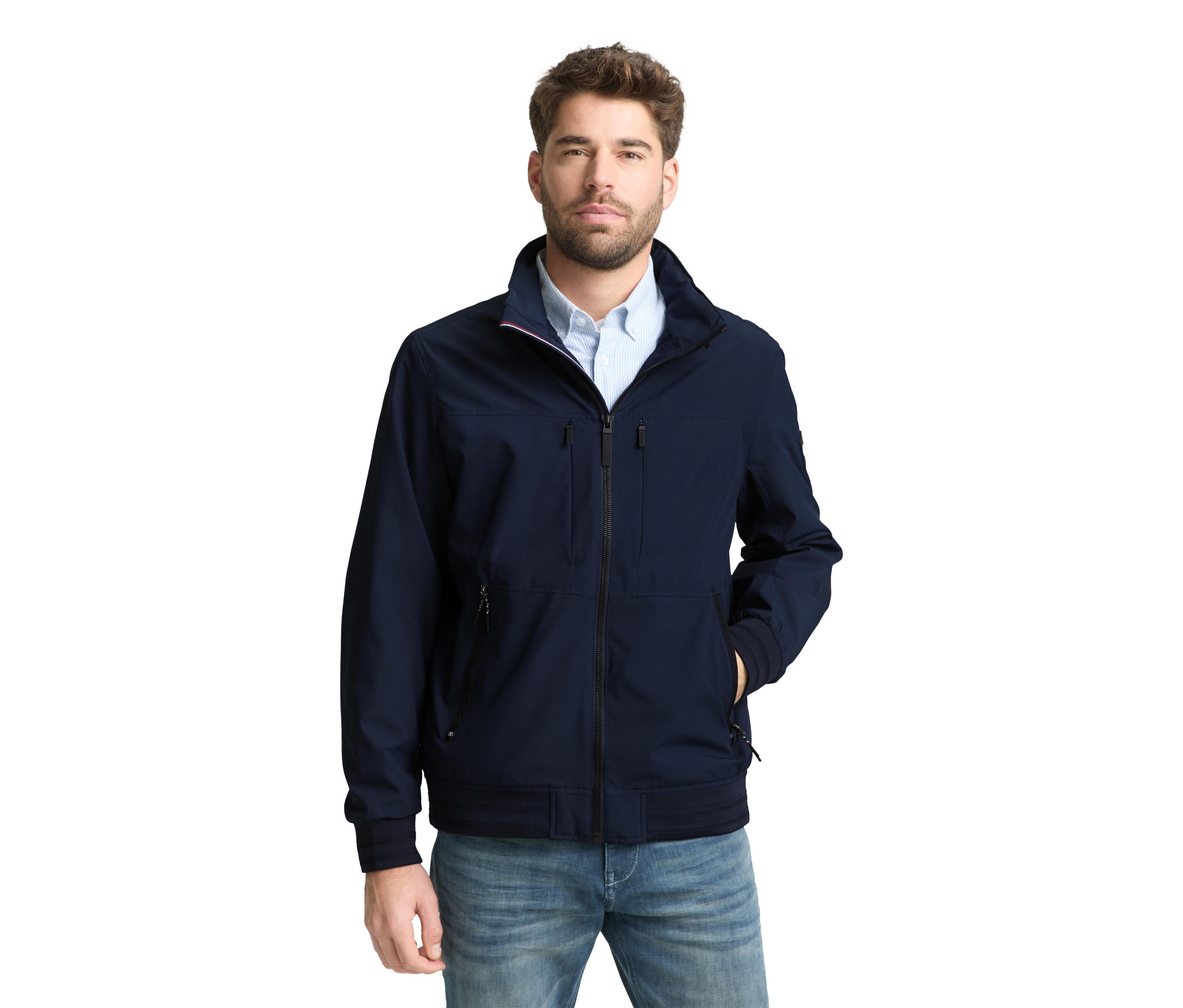 Szakállas férfi sötétkék kabátot és farmert visel.