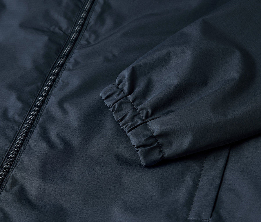 Egy sötétkék kabát részletfotója cipzárral és gumírozott mandzsettákkal.
