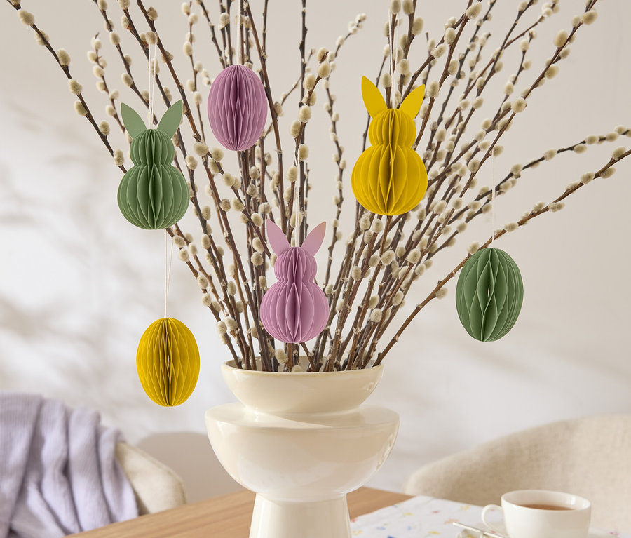 Dekoratív húsvéti ágak lógó papírdíszekkel nyúl és tojás formában sárga, zöld és lila színben egy vázában.