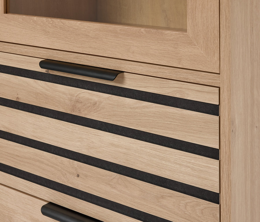 Egy világosbarna fa szekrény részletfotója fekete vízszintes ékezetes fiókokkal és fekete vízszintes fogantyúkkal.
