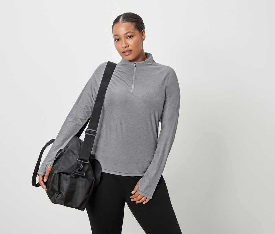Nő szürke, hosszú ujjú felsőt és fekete sporttáskát visel a vállán.