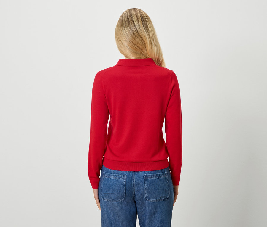 Hátulnézet egy szőke hajú nőről, aki piros pulóvert és kék farmert visel.