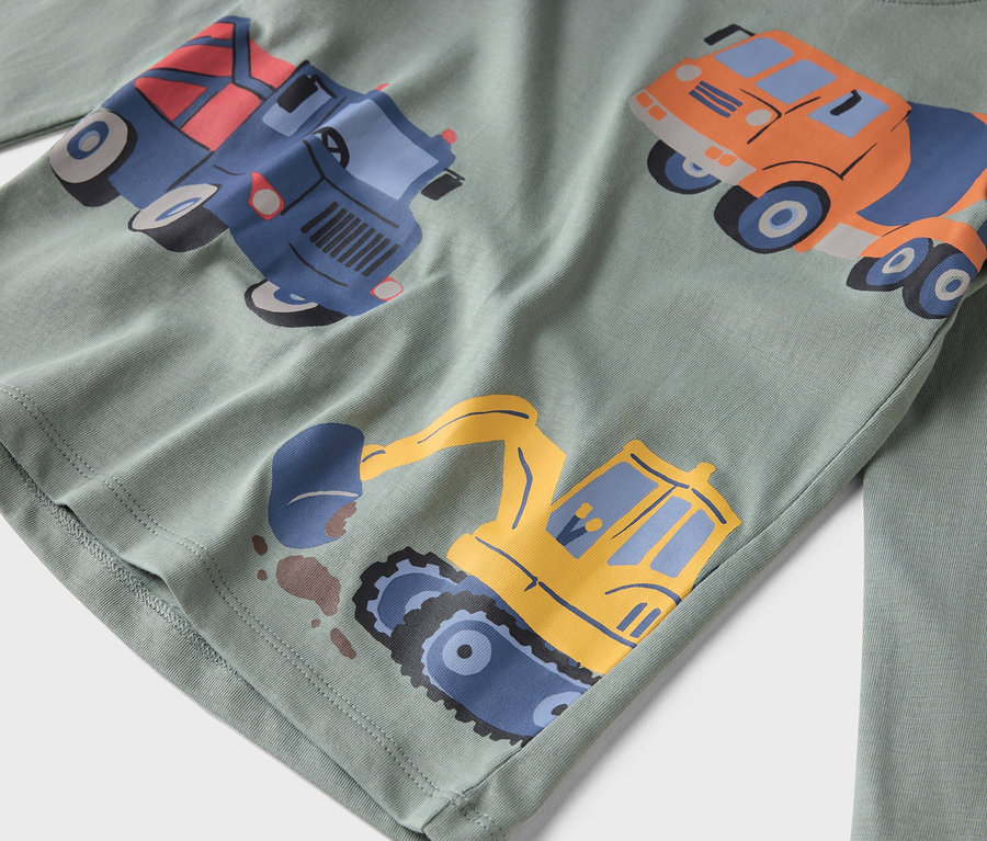 Egy világoszöld, hosszú ujjú póló közelképe, építőipari járművekkel nyomtatva.