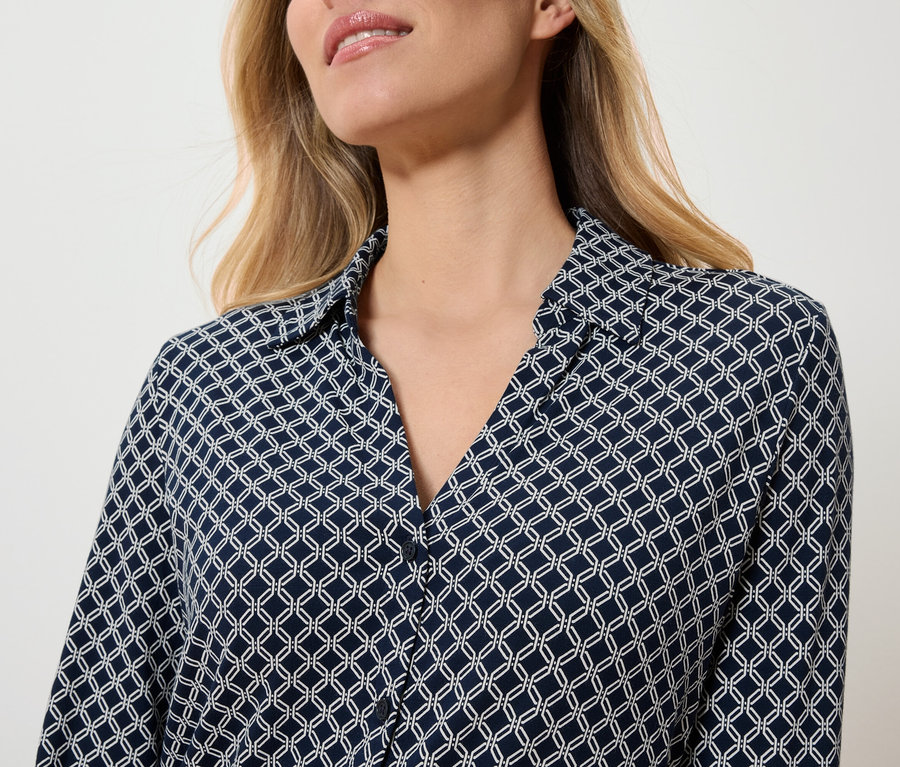 Egy nő felsőteste sötétkék, fehér geometriai mintás blúzban.