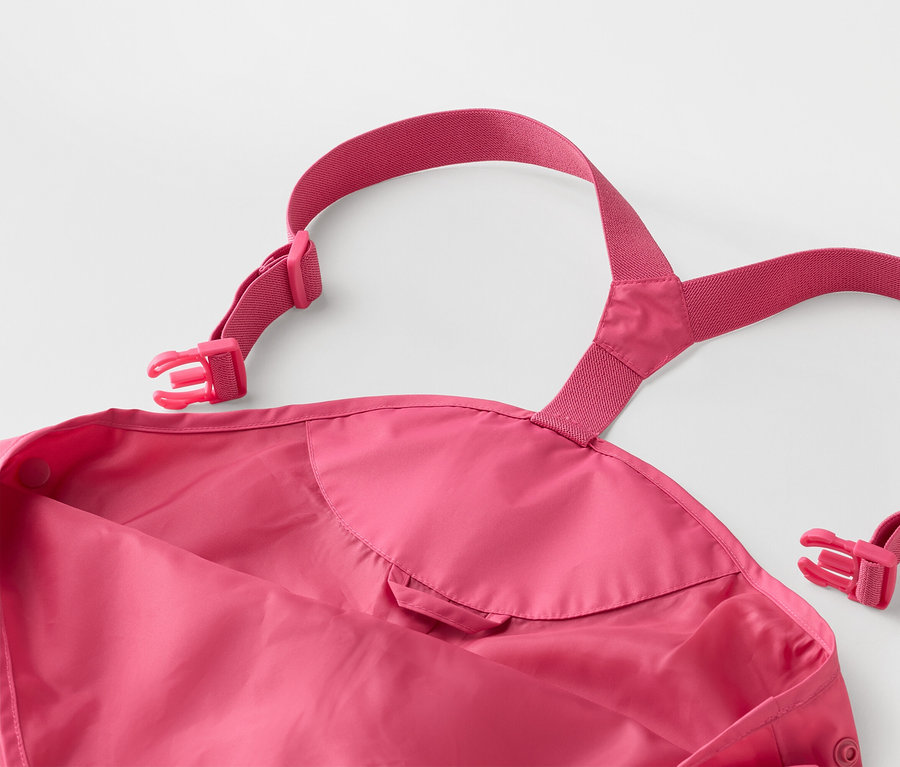 Egy rózsaszín, állítható pántokkal és csatokkal ellátott gyermek esőnadrág közeli képe fehér háttérrel.