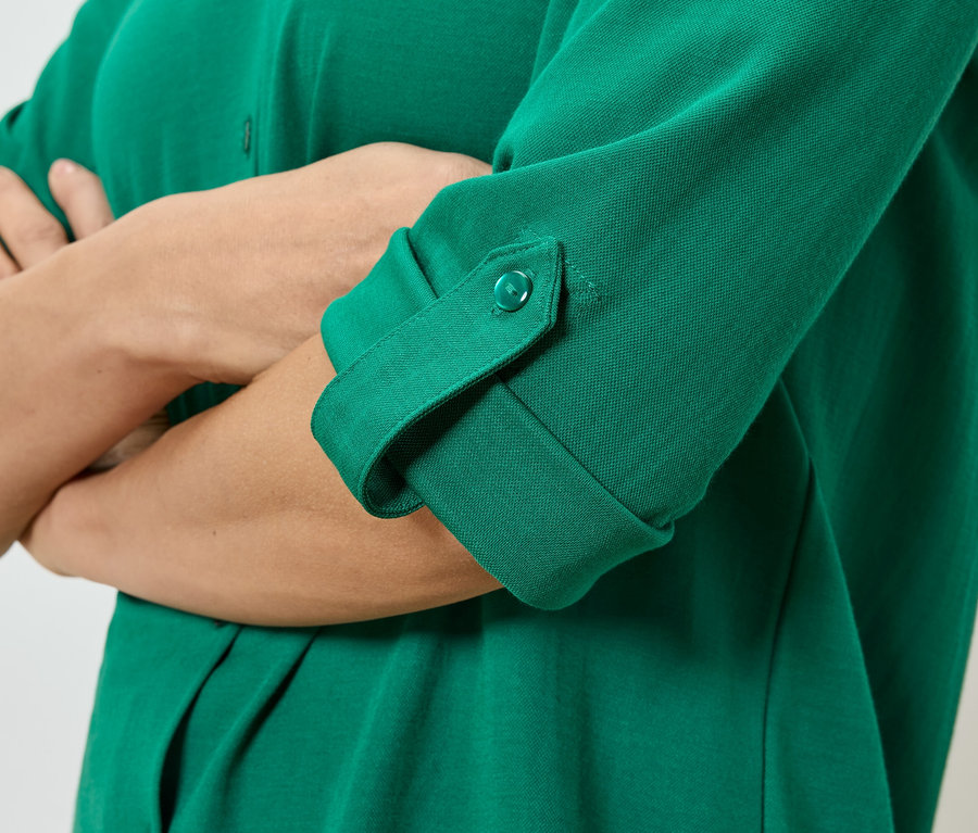 Egy személy közeli képe keresztbe tett karokkal, zöld, gombos ingben, felhajtott ujjal.