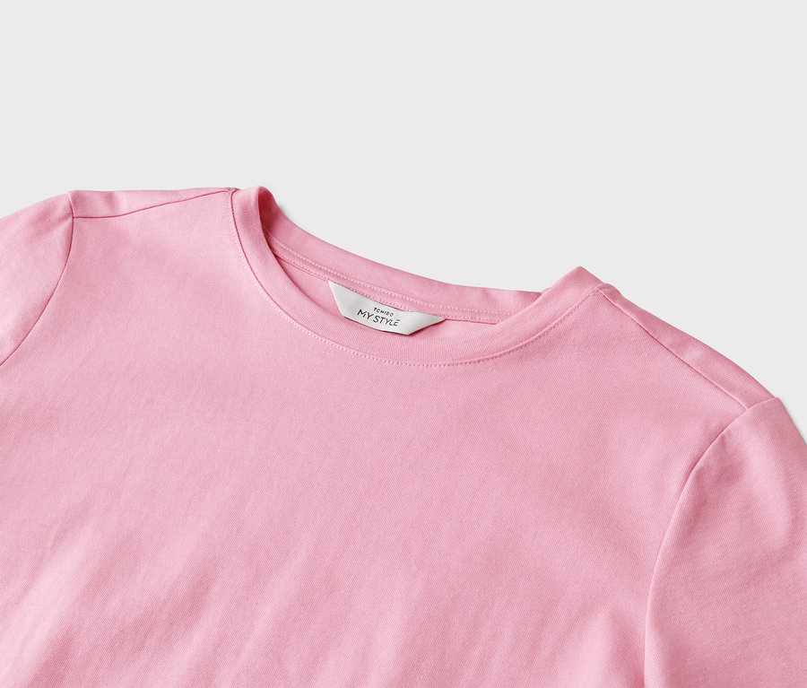 Közeli kép egy világos rózsaszín, kerek nyakú pólóról, melyen egy „Tchibo My Style” feliratú fehér címke található.