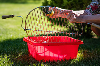 A grill megfelelő tisztítása: két kéz egy piros négyzet alakú műanyag tálban vízzel tisztítja a grillrácsot.