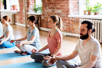 A megfelelő jóga ruházat: Egy fiatalokból álló csoport a jógaszőnyegeiken ül és meditál.