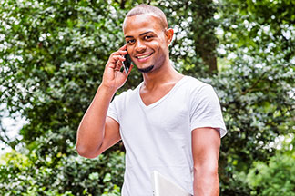 Egy fehér, V-nyakú pólót viselő fiatal férfi egy parkban telefonál.